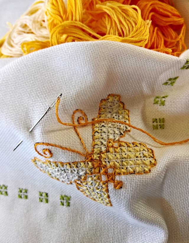 Small cross-stitch pieces of a cat and a fox beside spools of embroidery floss and felt owls